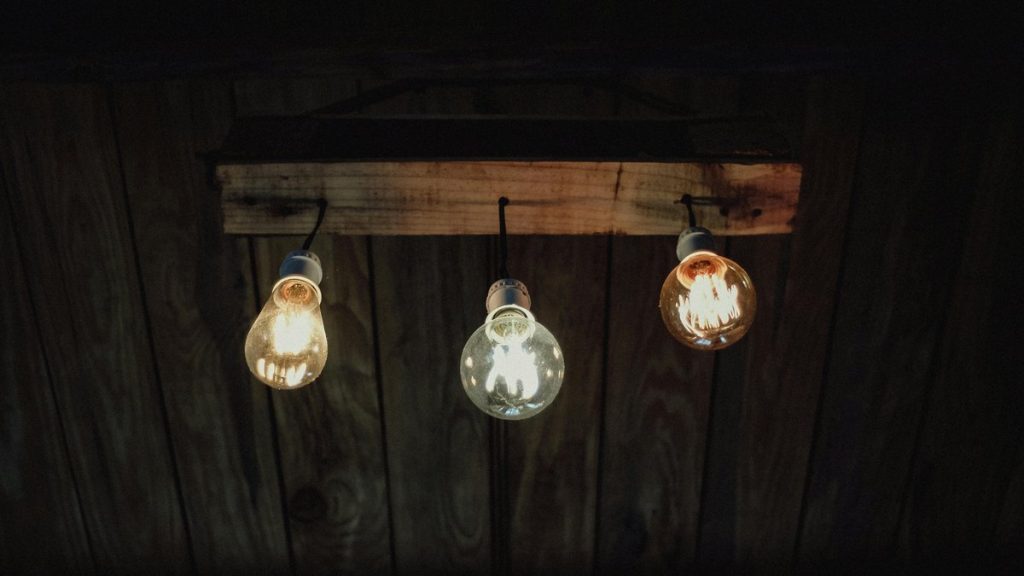 Three rustic light bulbs illuminate from wooden fixture on ceiling, creating a warm, vintage ambiance.