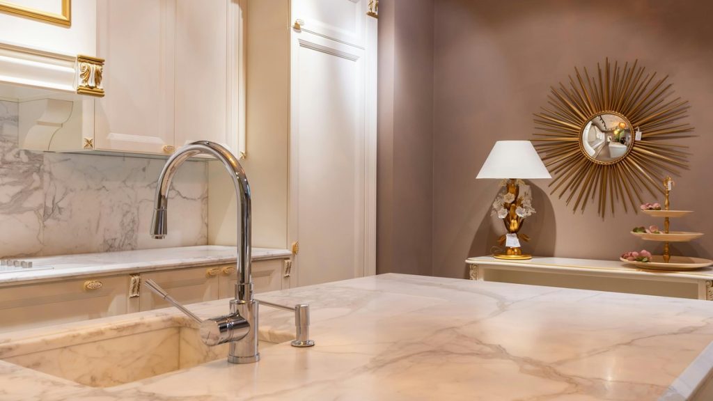 Sink with faucet on marble counter in modern stylish kitchen with white cabinets and glowing lamp near decorations in apartment