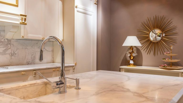Sink with faucet on marble counter in modern stylish kitchen with white cabinets and glowing lamp near decorations in apartment