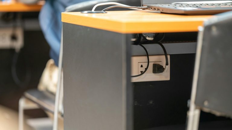 A clean office workspace featuring a desk, laptop, and hidden power cord management.