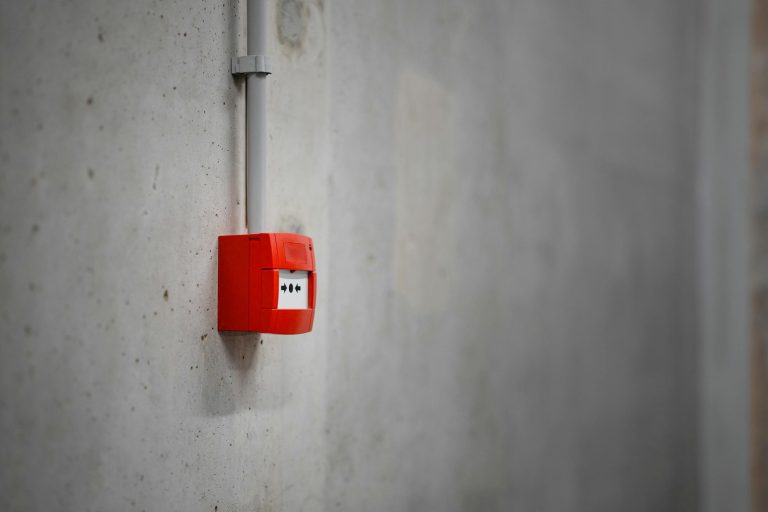 A red alarm box mounted on a gray concrete wall, offering urban security.