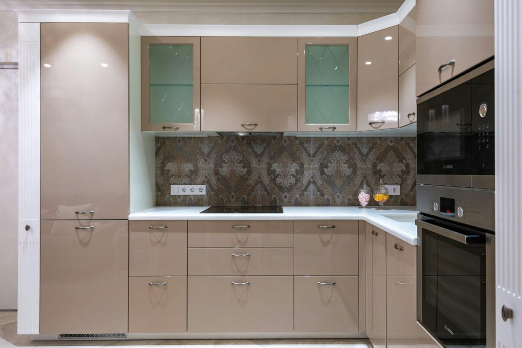 Contemporary kitchen with beige glossy cabinets and built in oven and microwave in column under bright lights