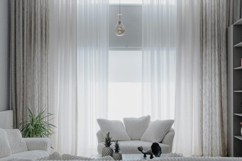 A minimalist living room with soft white sofas and large curtains, creating a cozy atmosphere.