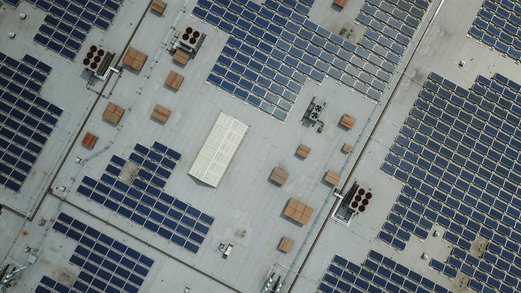 High-angle aerial shot of a large rooftop solar panel array on an industrial building.