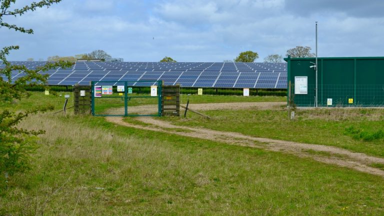 Large solar power station with panels in an open green field under a cloudy sky.